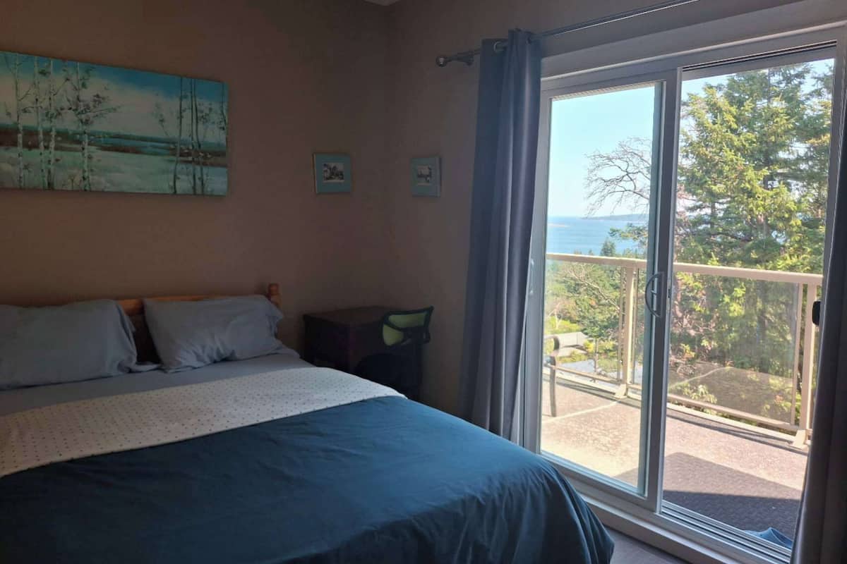 Un dormitorio con cama, un cuadro y vistas al exterior a través de un ventanal corredera.
