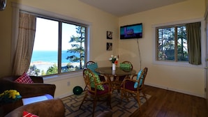 A cozy living room with a dining area, large windows with ocean views, and a flat-screen TV mounted on the wall. - Gibralter Rock Ocean View B&B (Nanaimo)