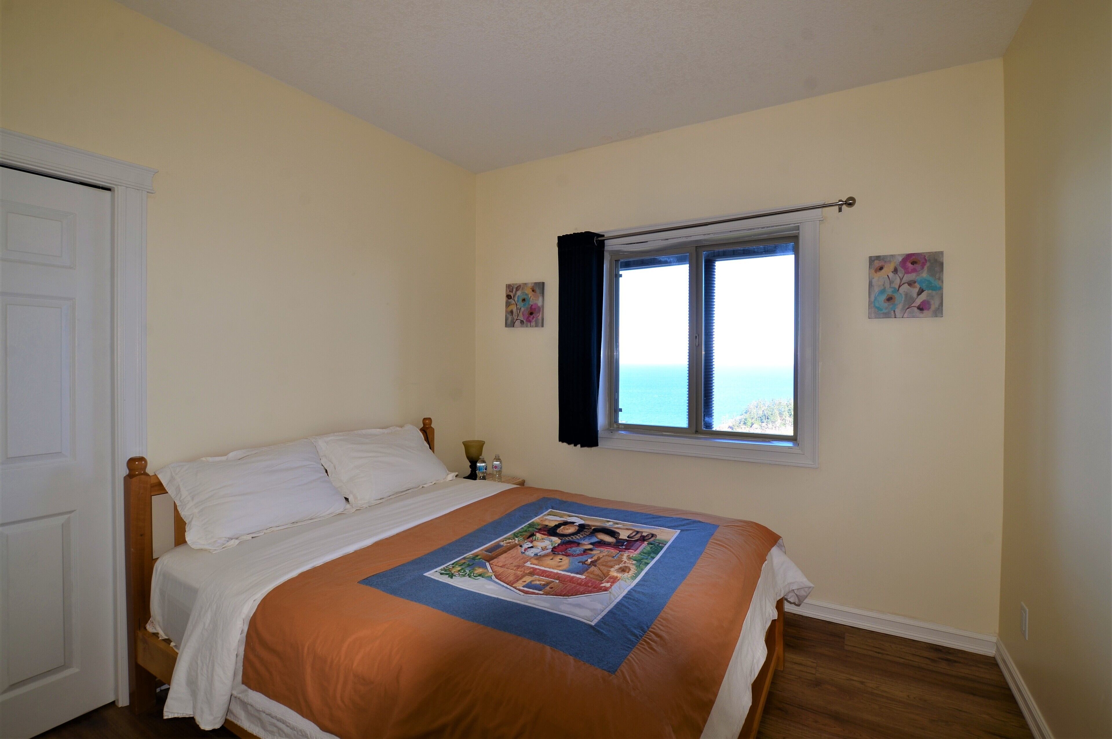A bedroom with a bed, a window with a view, and two paintings on the wall.