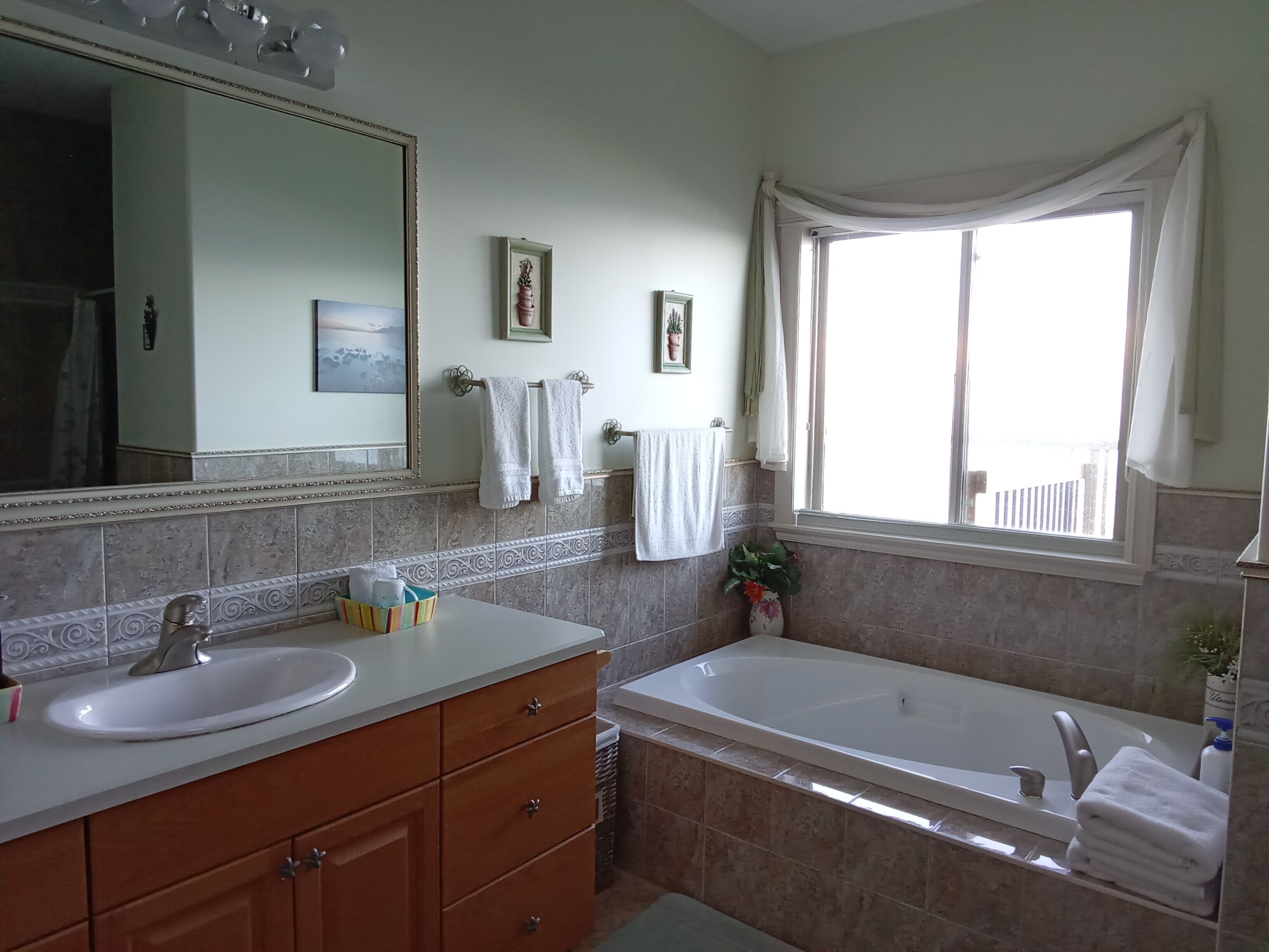 Ein Badezimmer mit einem großen Spiegel, zwei Waschbecken, einer Badewanne und einem Fenster mit Vorhängen.