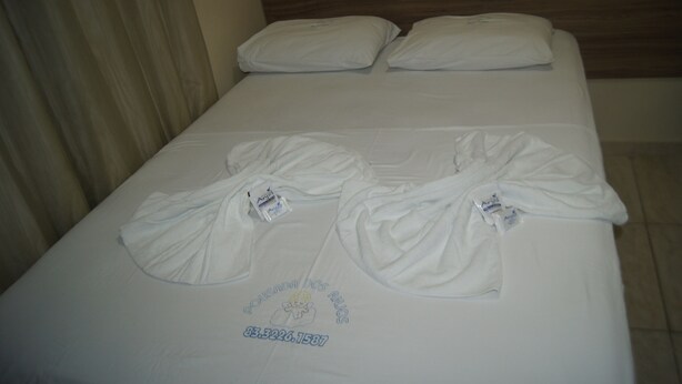 Een bed met twee witte kussens en twee witte badjassen.