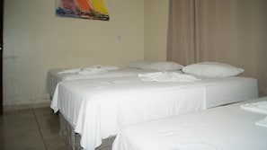 Habitación de hotel con dos camas, ropa de cama blanca, una cortina color beige y un cuadro de colores en la pared.