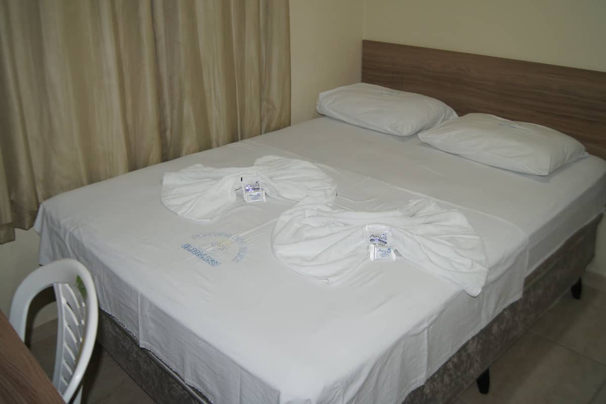 Un lit bien fait, avec du linge de lit blanc et deux oreillers, une tête de lit en bois et une chaise blanche.