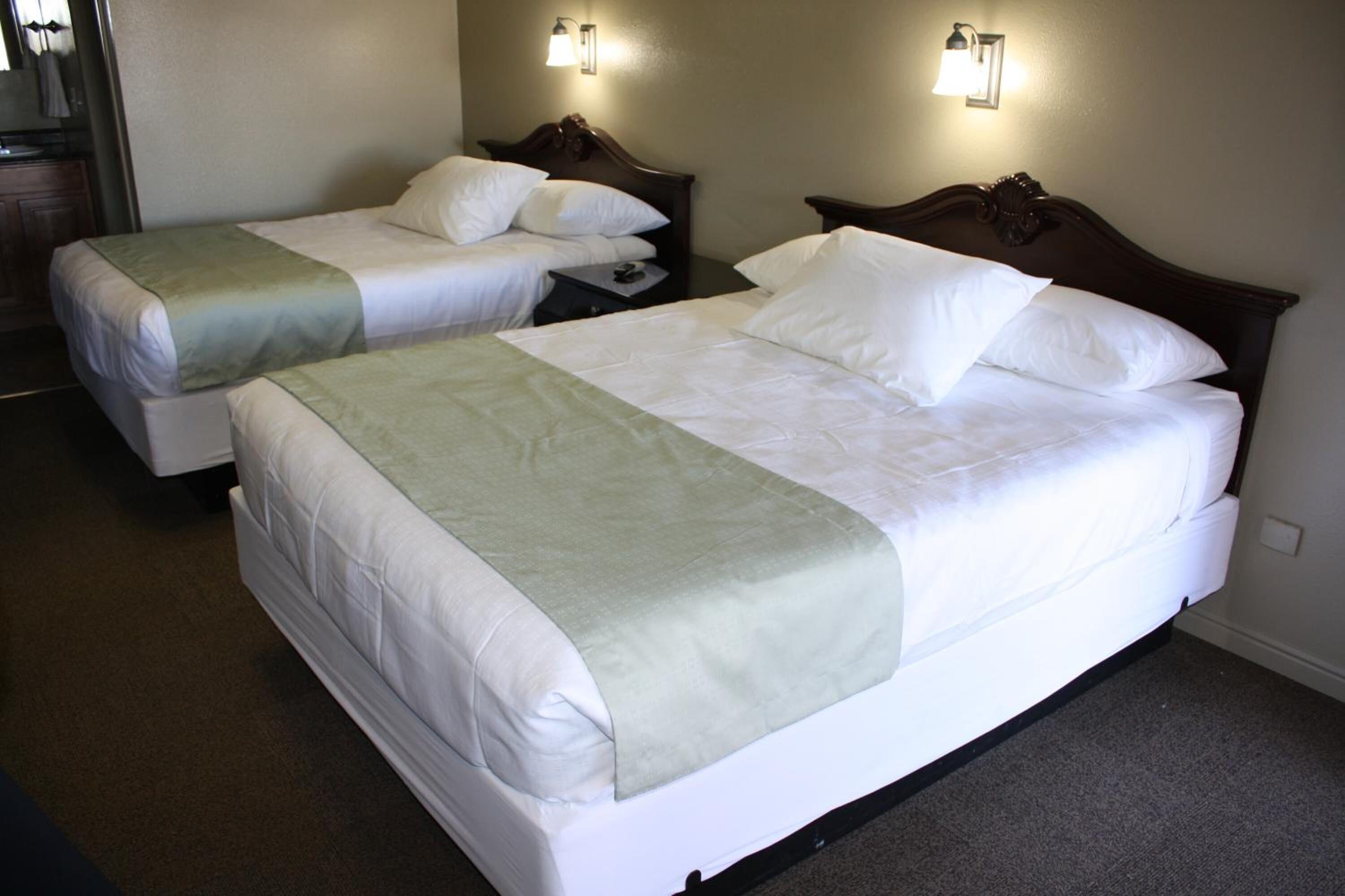 Two single beds with white linens and green throw blankets, wooden headboards, and wall-mounted reading lamps.