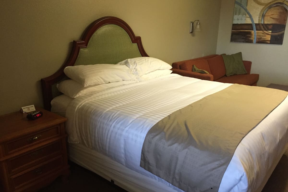 A neatly made bed with white linens, a wooden headboard, and a bedside table with a clock.
