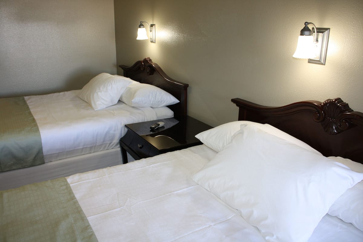 A hotel room with two single beds, a nightstand, and two wall-mounted lamps.