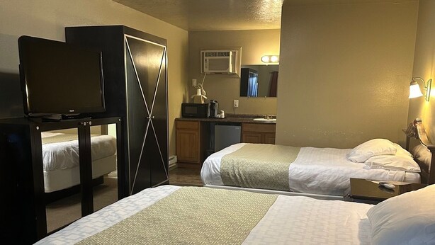A hotel room with two beds, a desk, a wardrobe, a television, a mirror, and a bathroom with a sink and mirror. - Gateway Inn (Lyman)