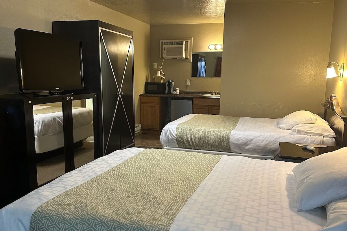 A hotel room with two beds, a desk, a wardrobe, a television, a mirror, and a bathroom with a sink and mirror.