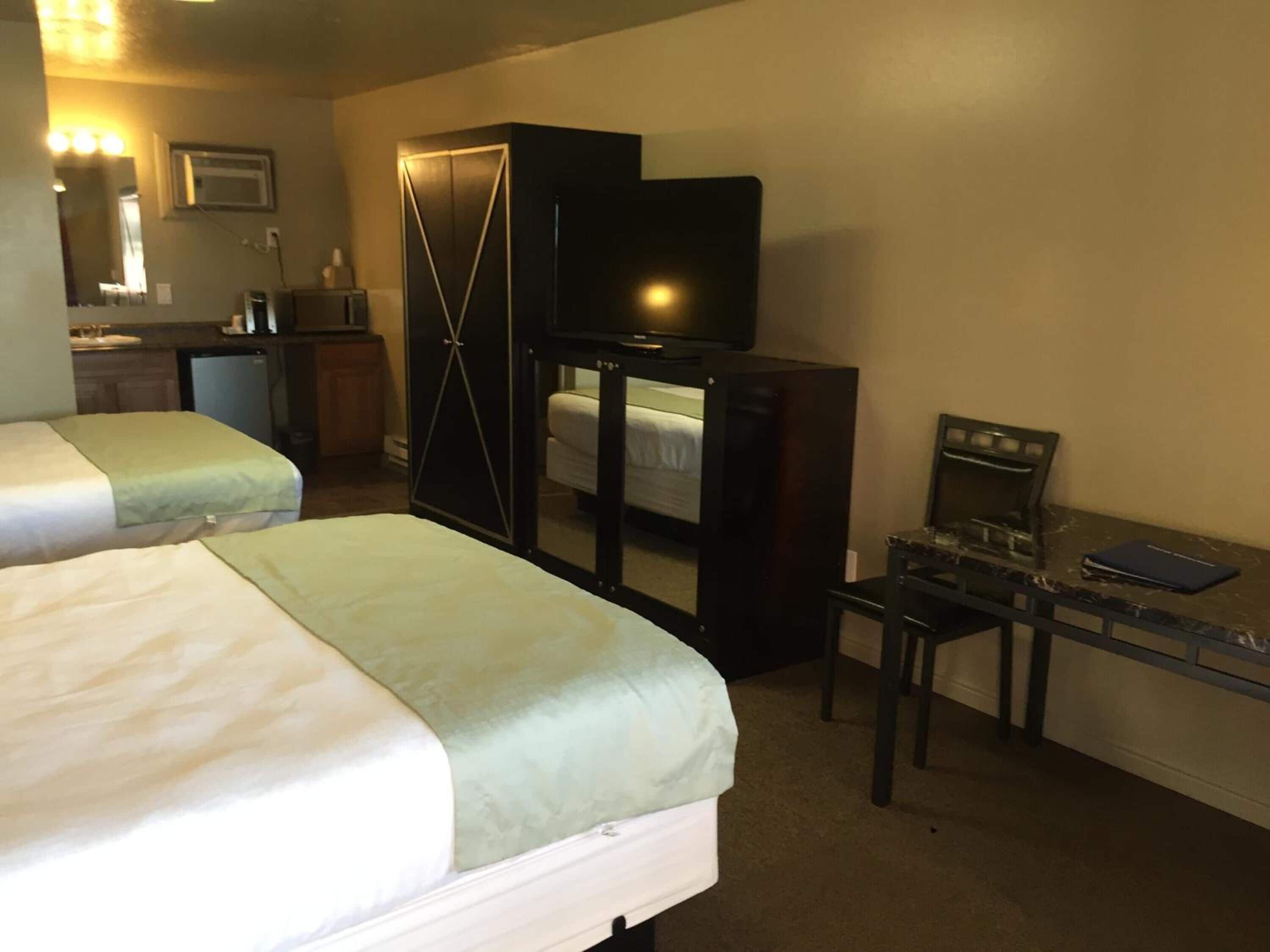 A hotel room with two beds, a desk, a television, a mirror, and a kitchenette.
