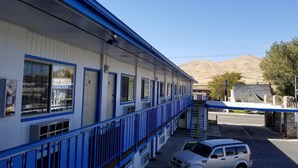 A motel with a blue and white exterior, a covered parking area, and a mountainous backdrop. - Regency Inn (Winnemucca)