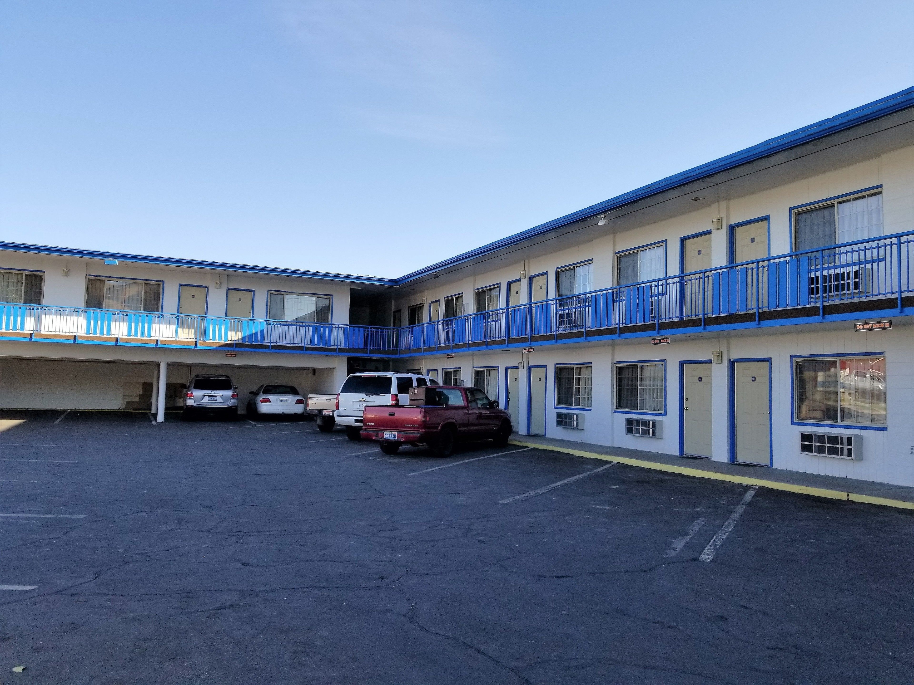 A motel with a parking lot, multiple rooms, and a blue railing on the balconies.