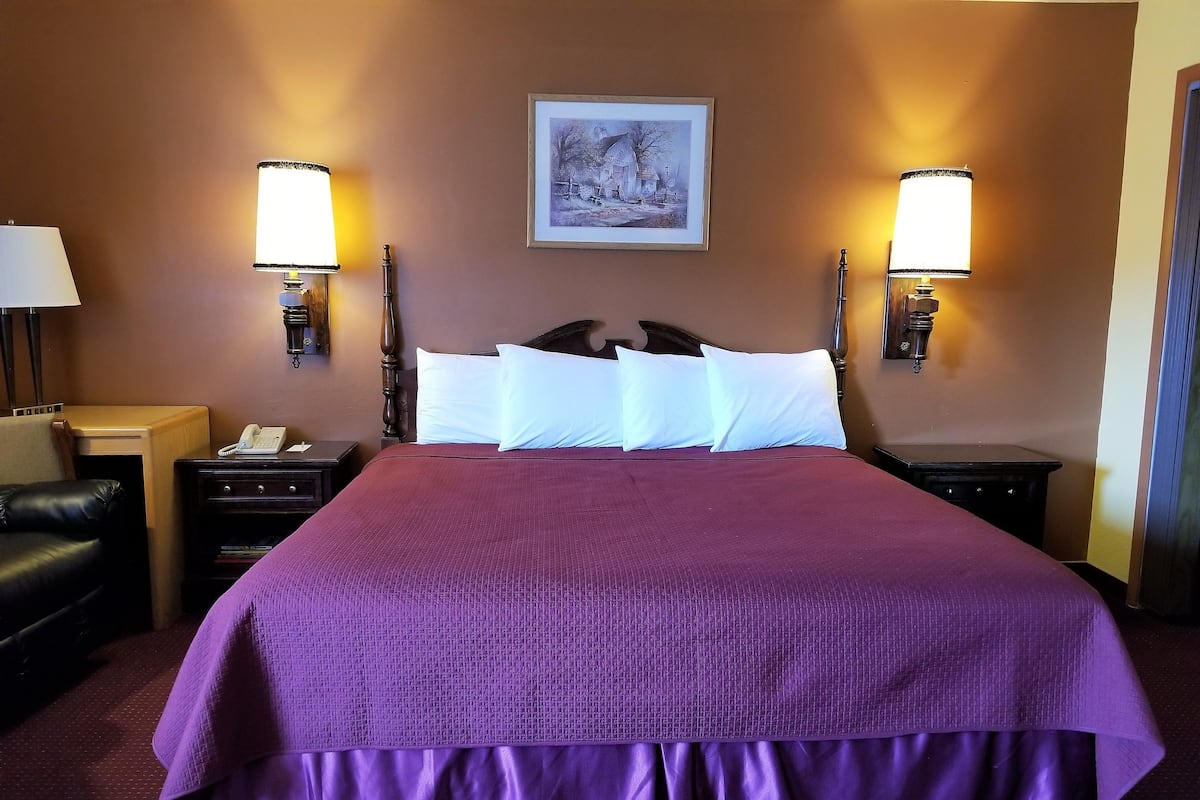 A hotel room with a large bed, two bedside lamps, a nightstand with a phone, and a framed picture on the wall.
