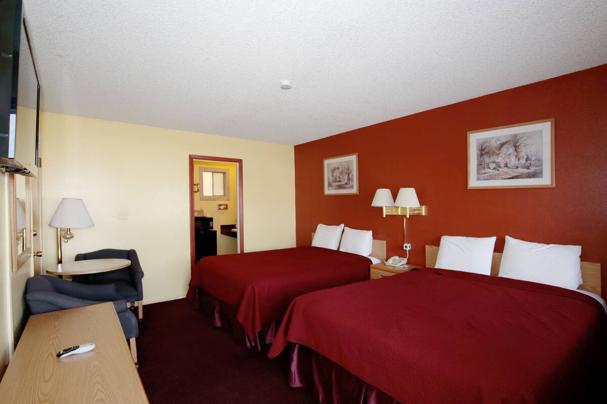 A hotel room with two beds, a desk, a chair, a lamp, and a painting on the wall.