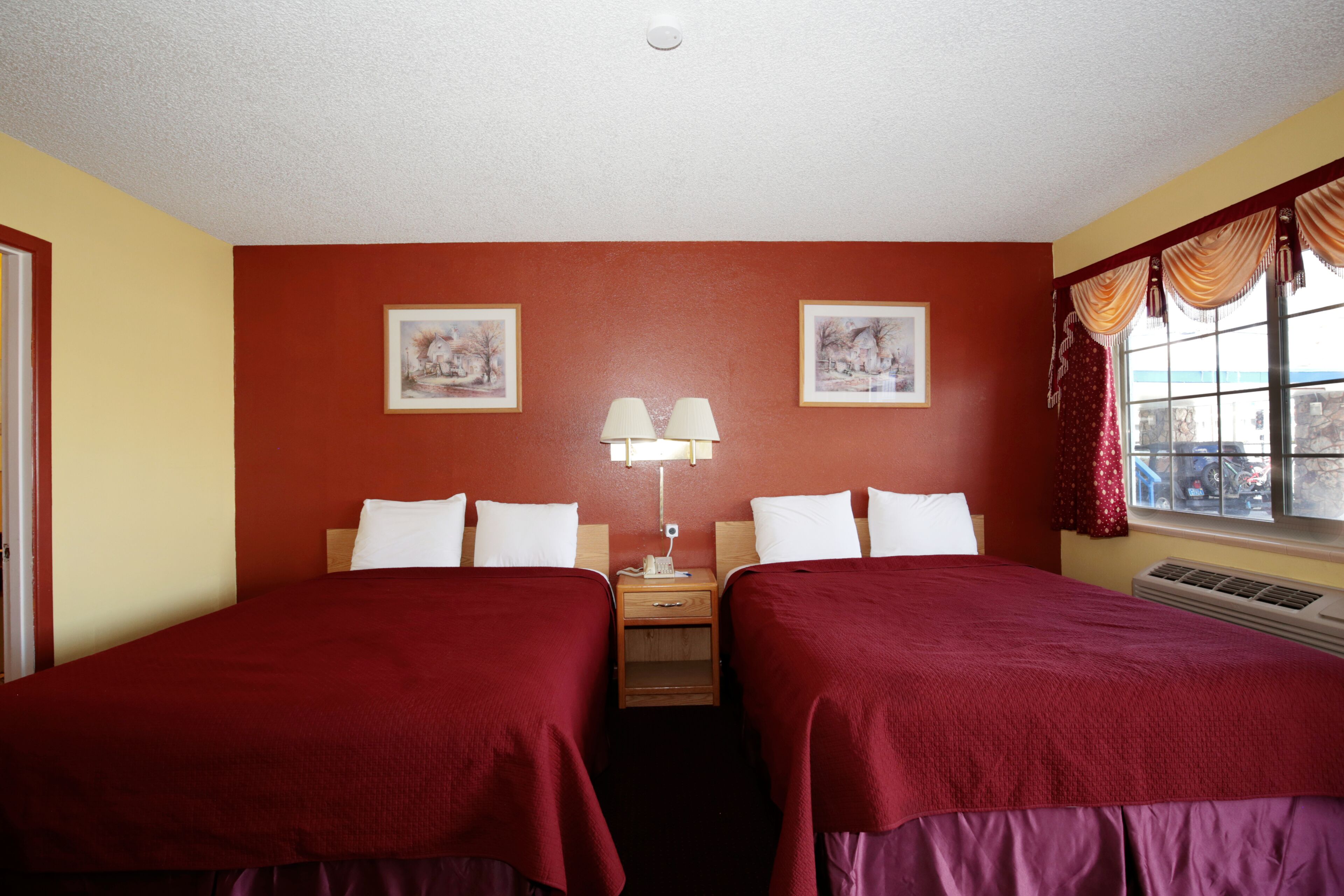 A hotel room with two beds, a nightstand with lamps, and two framed pictures on the wall.