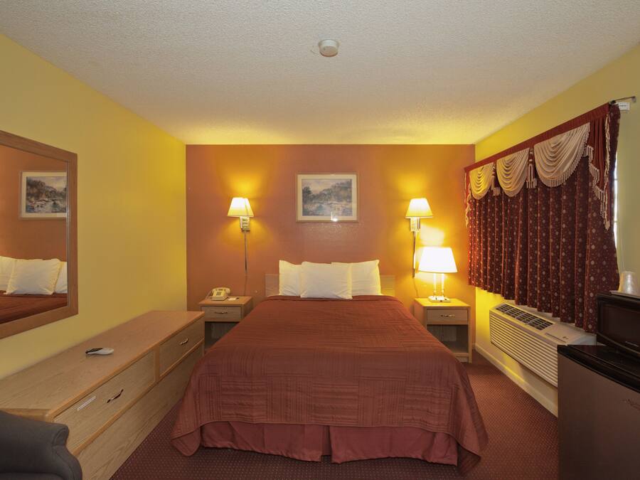 Habitación de hotel con una cama grande, dos mesitas de noche con lámparas, un aparador, un escritorio, un espejo y un refrigerador.