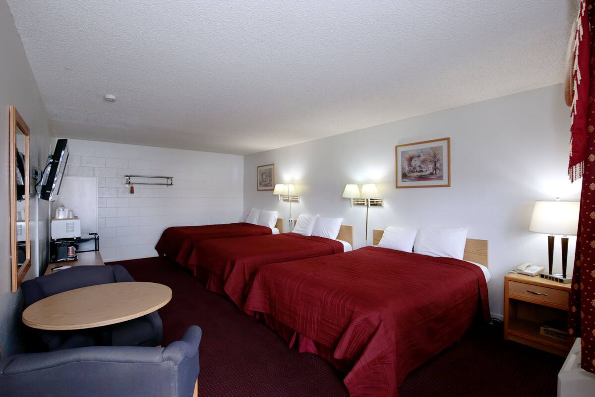 A hotel room with two beds, a small table, a chair, a desk with a lamp, a telephone, and a picture on the wall.