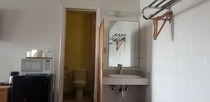 A compact bathroom with a toilet, a sink, and a mirror. A microwave is placed on a small table beside the toilet.