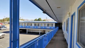 A motel with a covered walkway, a parking lot, and a building with blue trim. - Regency Inn (Winnemucca)