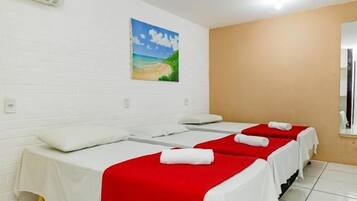 A hotel room with three beds, white walls, a painting of a beach, and a window.