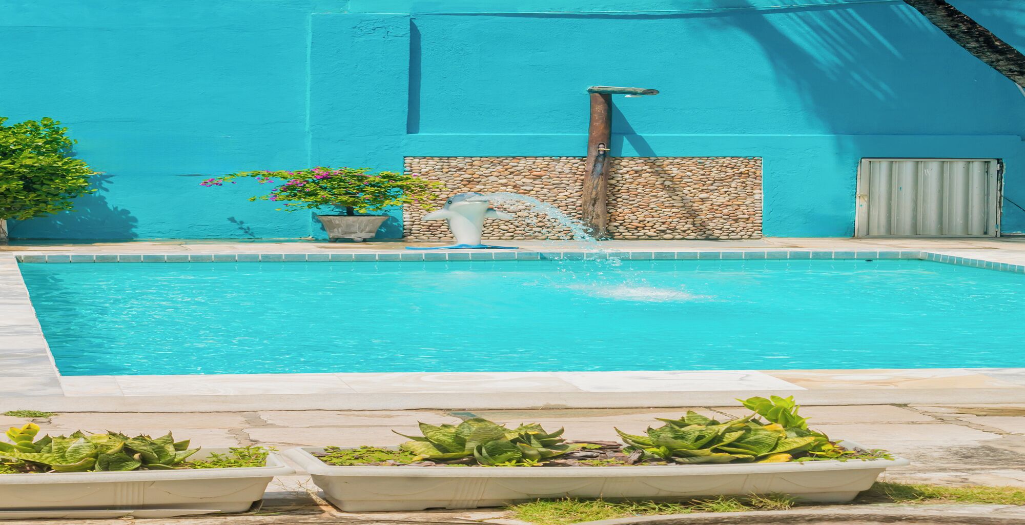 Une piscine rectangulaire avec un mur en pierre et une structure en bois d’un côté.