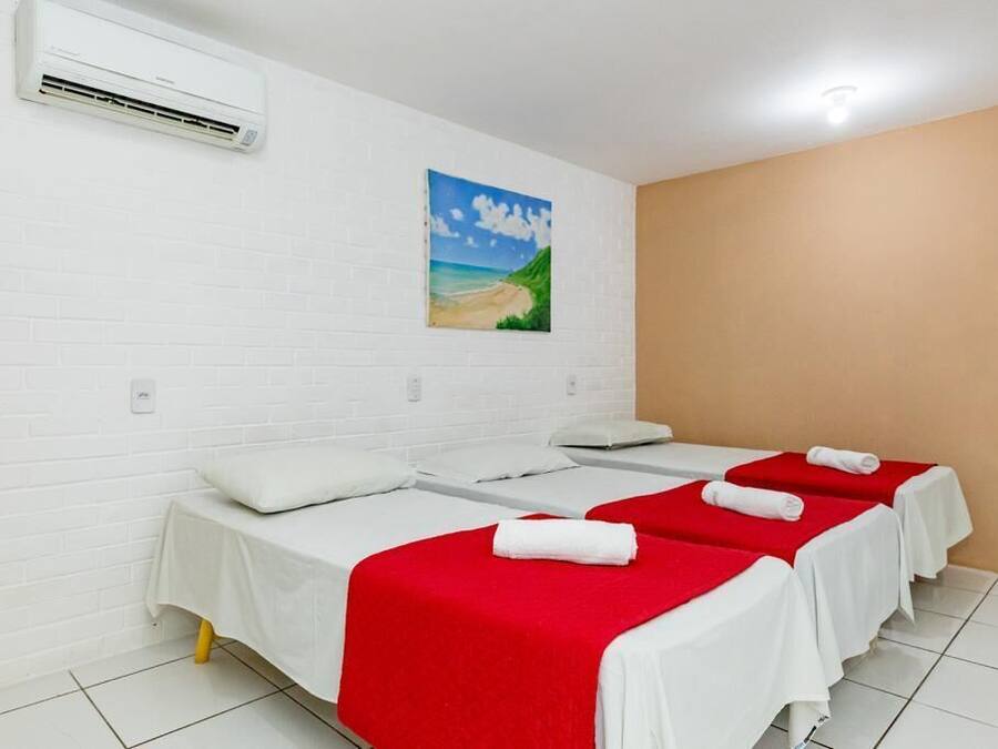 Una habitación con tres camas, paredes blancas, un cuadro de playa y un equipo de aire acondicionado.
