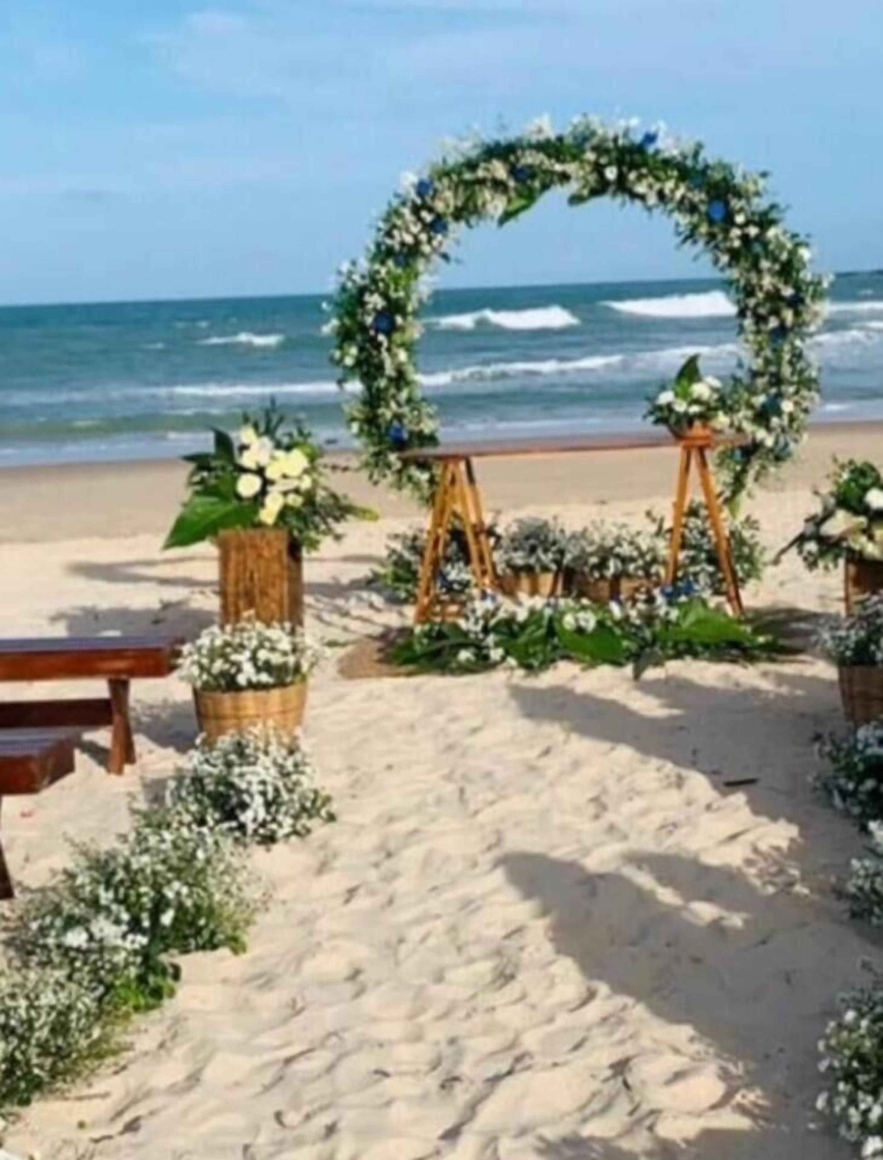A beach wedding setup with a floral arch and wooden stands.
