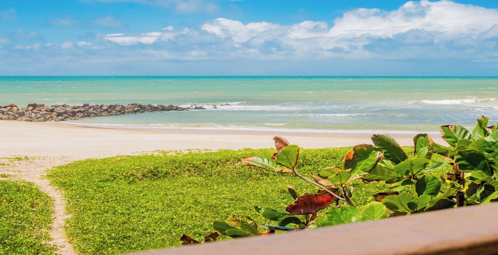 A beach with a clear view of the ocean and a rocky outcrop in the distance.