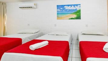 Habitación de hotel con tres camas, cada una con colcha roja y almohadas blancas, y un cuadro con una escena de playa en la pared.