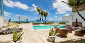 A pool area with lounge chairs, a swing set, and a view of the ocean. - Hotel Paraíso Natal (Natal)