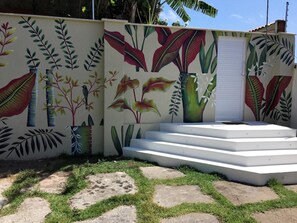 A building with a mural of tropical plants and a set of white steps leading to a door. - La Réserve Design Villas (Tibau do Sul)