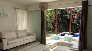 A modern living room with a sofa, a coffee table, and a view of a pool and garden. - La Réserve Design Villas (Tibau do Sul)