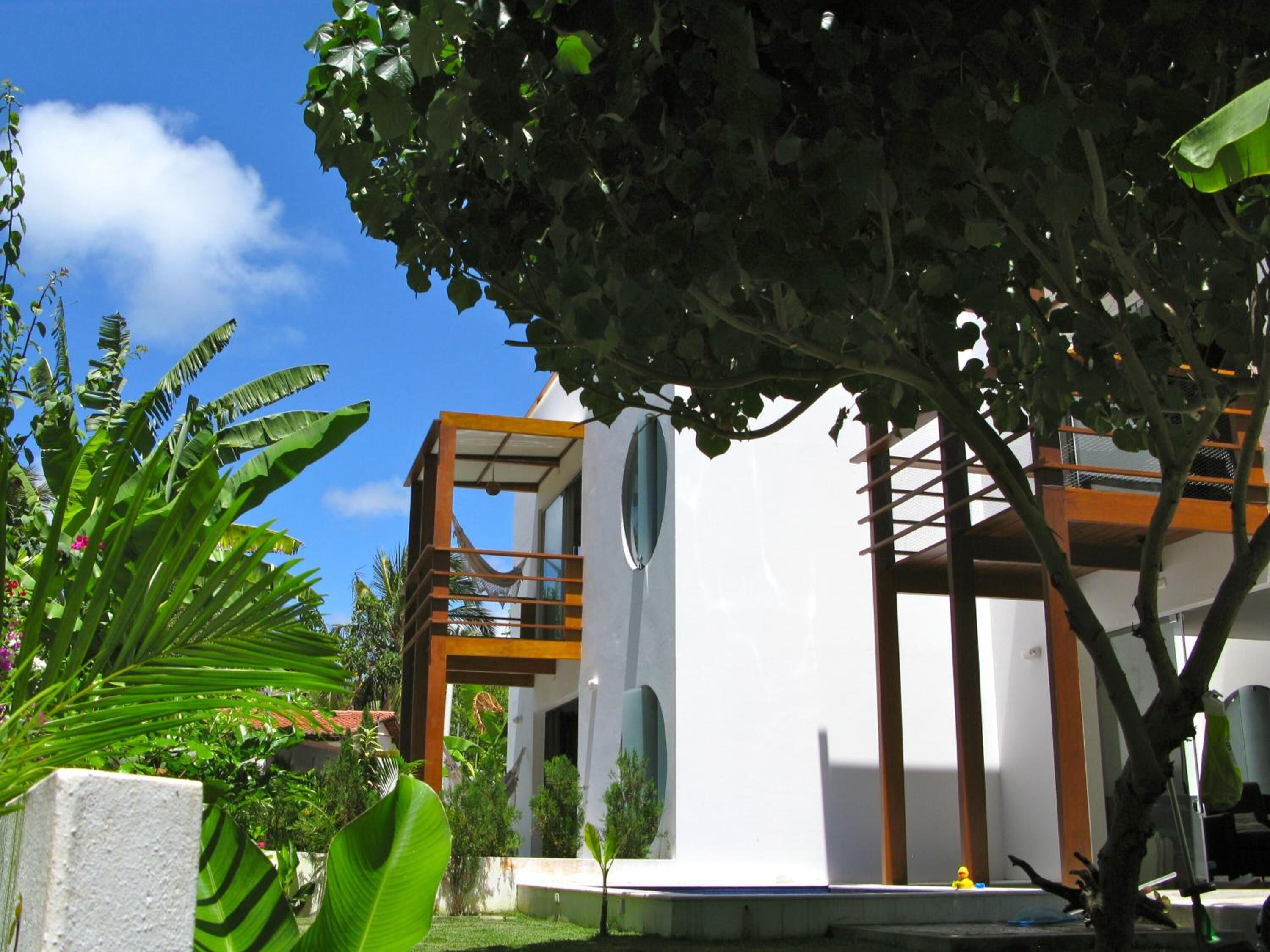 A modern building with a balcony and a circular window, surrounded by lush greenery.