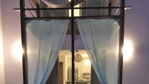A modern indoor pool with a blue-lit water surface, two cushioned seating areas with pillows, and sheer blue curtains framing the view into a well-lit interior space. - La Réserve Design Villas (Tibau do Sul)