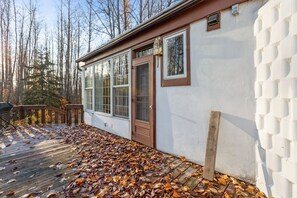 A house with a wooden deck covered in fallen leaves, a white exterior wall, and a brown door. - EQC Hotel 127 (Région Test)