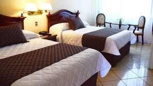 Une chambre d’hôtel avec deux lits, chacun recouvert d’une courtepointe matelassée, dotée de lampes de chevet et comprenant une petite table avec une chaise.