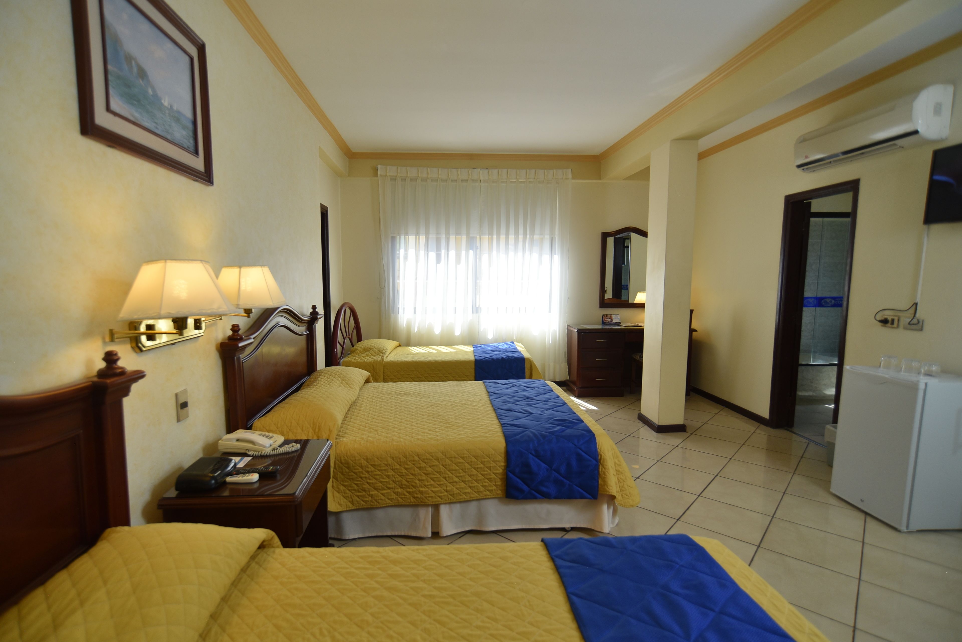 A hotel room with two beds, a desk, a telephone, and a refrigerator.