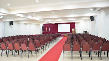 A conference room with rows of chairs, a red carpet, a podium, and a screen at the front.