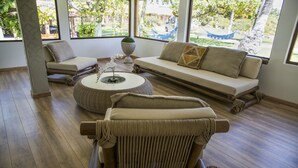 A spacious room with a wooden floor, a sofa, a chair, and a round table. - Fiore Resort e Residence (Paripueira)