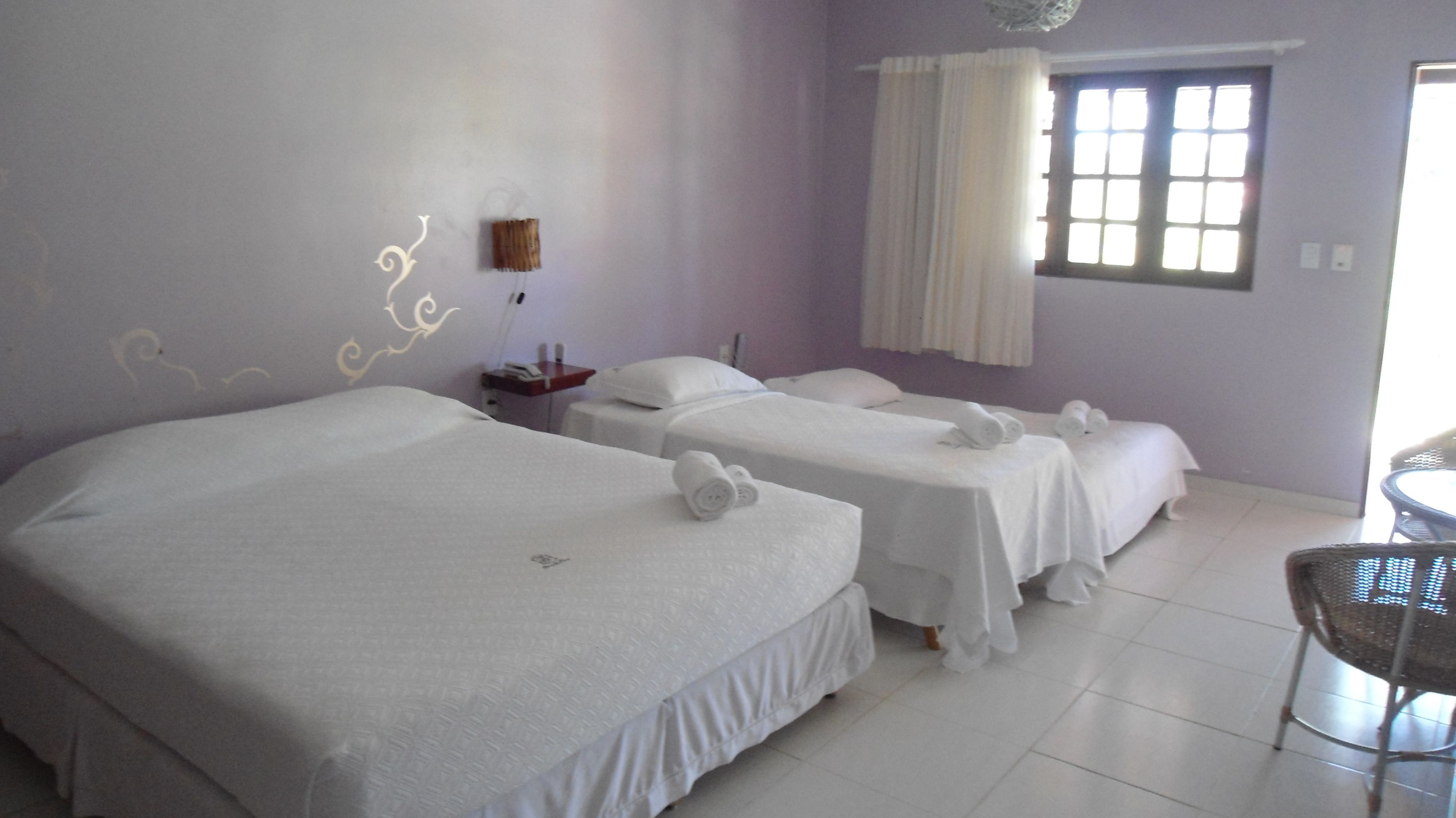 A hotel room with three single beds, a small table, and a chair.