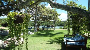 A hammock under a tree, a wooden bench, and a grassy area with a lake in the background. - Fiore Resort e Residence (Paripueira)