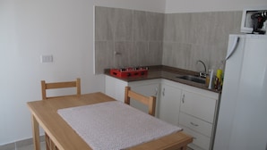 Une cuisine de taille réduite, avec une table en bois, des chaises, un évier et un réfrigérateur.