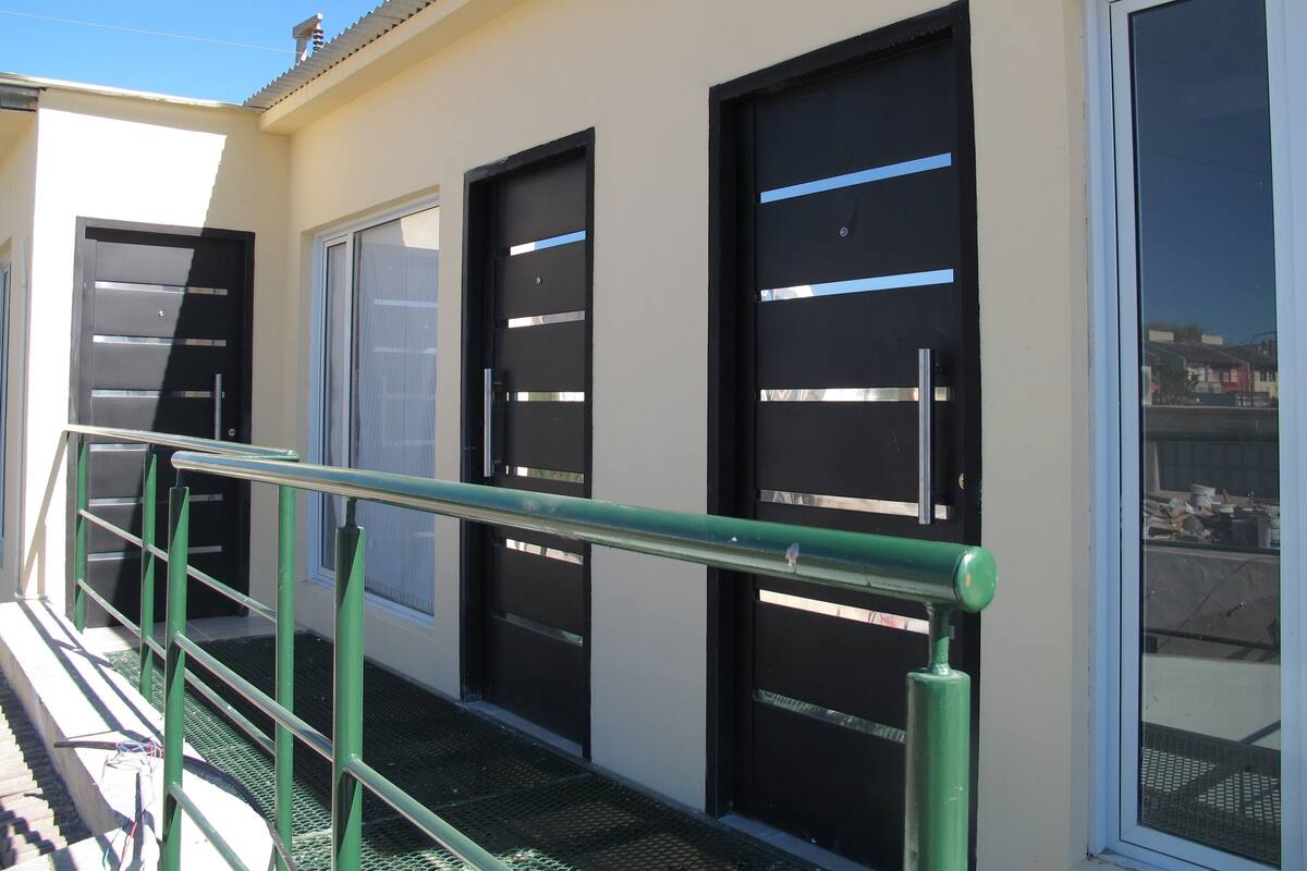 A building with a green metal railing, black doors with horizontal metal bars, and a window with a metal grid.