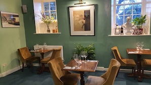 A dining area with wooden tables and chairs, framed artwork on the walls, and a window with a view of trees. - Lowbyer Manor Country House (Alston)