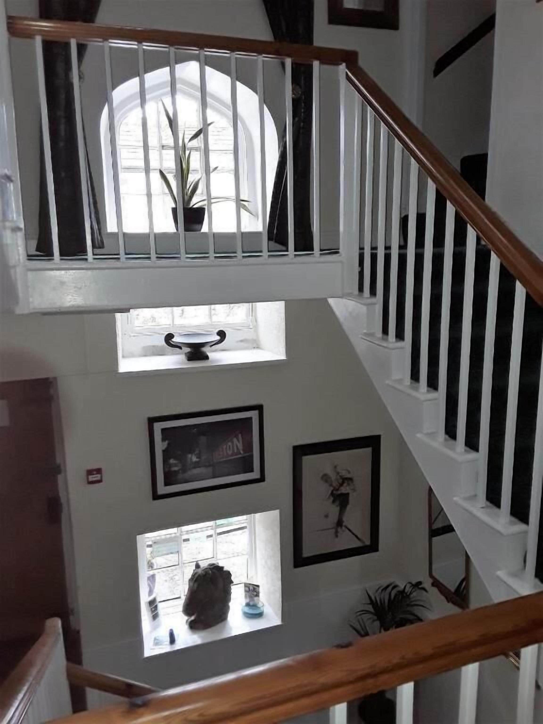 A multi-level interior with a wooden staircase, white railings, and a view of a window with a plant.