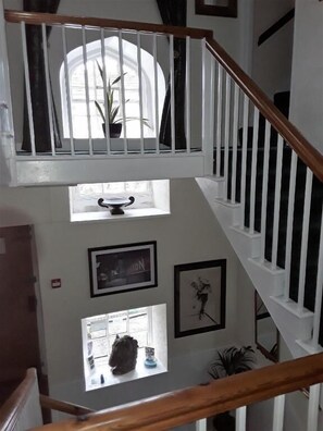 A multi-level interior with a wooden staircase, white railings, and a view of a window with a plant. - Lowbyer Manor Country House (Alston)