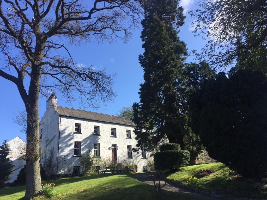 A white building with multiple windows and a door, surrounded by trees and a well-maintained lawn.