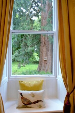 A window seat with a cushion featuring a bird design, a view of a tree, and a glimpse of a grassy area outside. - Lowbyer Manor Country House (Alston)