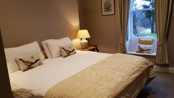 Habitación de hotel con una cama grande, una mesita de noche con lámpara y una ventana con cortinas.