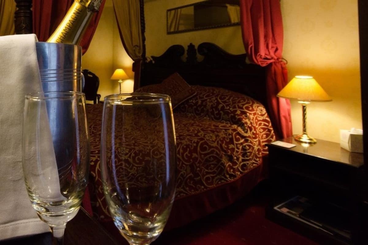 A four-poster bed with red curtains, a bedside lamp, and a bottle of champagne.
