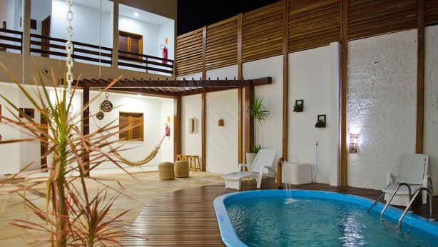 A swimming pool area with a wooden deck, lounge chairs, and a small indoor pool.